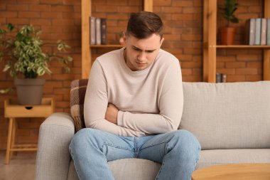 Evdeki kanepede karın ağrısı çeken genç bir adam.