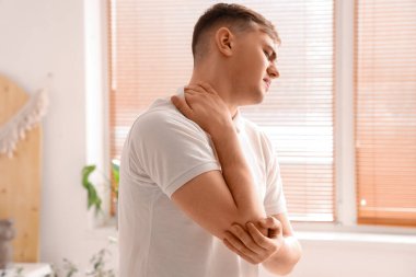 Yatak odasında boyun ağrısı çeken genç bir adam.