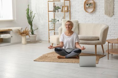 Evde laptopla meditasyon yapan olgun bir kadın. Online yoga dersleri