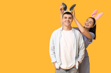 Sarı arka planda Paskalya tavşanı kulakları olan mutlu genç çift.