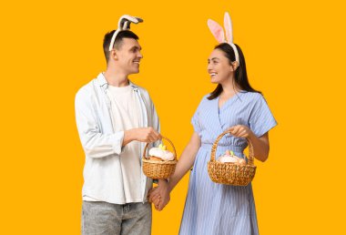 Paskalya sepetleri ve sarı arka planda tavşan kulakları olan mutlu genç çift.