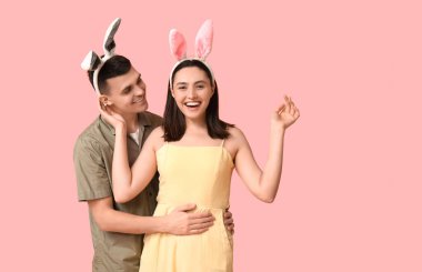 Pembe arka planda Paskalya tavşanı kulakları olan mutlu genç çift.