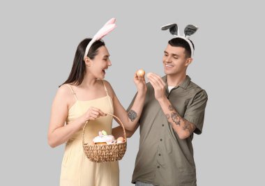 Paskalya sepeti ve gri arka planda tavşan kulaklı mutlu genç çift.