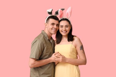 Pembe arka planda Paskalya tavşanı kulakları olan mutlu genç çift.