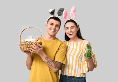 Paskalya sepeti, oyuncak tavşan ve gri arka planda tavşan kulaklı mutlu genç çift.