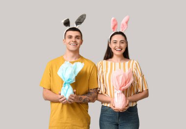 Paskalya tavşanı kulaklı mutlu genç çift ve gri arka planda hediyeler