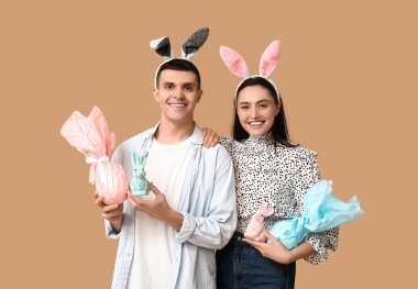 Paskalya hediyeli mutlu genç çift, oyuncak tavşanlar ve bej arka planda tavşan kulakları