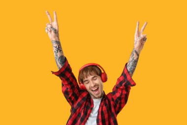 Kulaklıklı, sarı arka planda dans eden dövmeli genç adam.