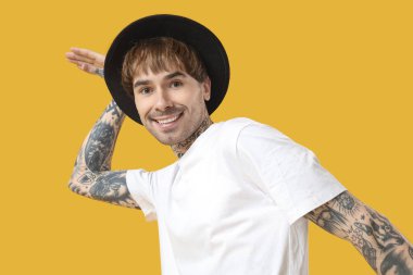 Sarı arka planda dans eden dövmeli genç adam.