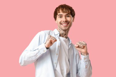 Pembe arka planda dans eden dövmeli genç adam.