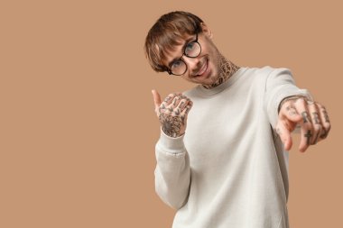 Genç dövmeli adam bej arka planda dans ediyor.