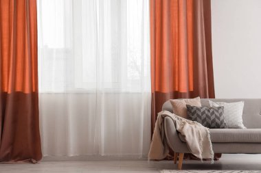 Oturma odasındaki kırmızı perdelerin yanındaki rahat kanepe.