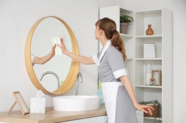 Genç oda hizmetçisi banyoda ayna temizliyor.