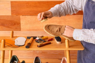 Erkek ayakkabıcı tahta arka planda ayakkabı fırçalıyor, yakın plan.