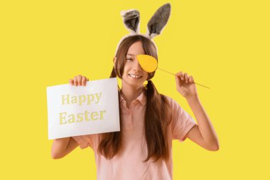 Paskalya tebrik kartı, tavşan kulağı ve sarı arka planda kağıt yumurtası olan tatlı küçük bir kız.