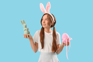 Paskalya tavşanı kulaklı, mavi arka planda yumurta ve oyuncak tavşanı olan tatlı bir kız.