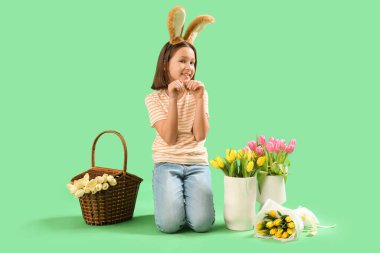 Paskalya tavşanı kulakları, sepeti ve yeşil arka planda çiçekleri olan tatlı küçük bir kız.
