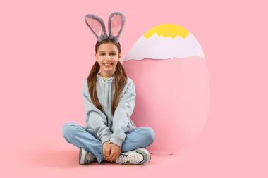 Paskalya tavşanı kulakları ve pembe arka planda büyük kağıt yumurtası olan tatlı küçük bir kız.