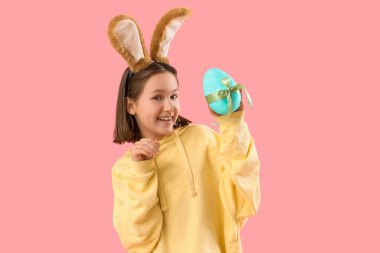 Paskalya tavşanı kulakları ve pembe arka planda yumurtası olan tatlı küçük bir kız.