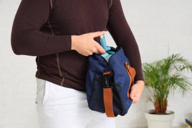 Spor salonunda spor çantasından astım spreyini alan genç adam, yakın plan.