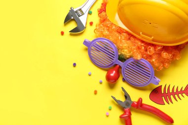 Palyaço peruğu, komik gözlükler ve sarı arka planda kağıt balık olan mekanik eşyalar. 1 Nisan Şaka Günü