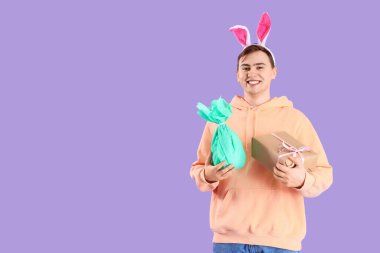 Mor arka planda hediyeleri olan tavşan kulaklı mutlu genç adam. Paskalya kutlaması