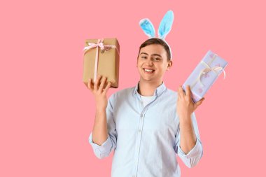 Pembe arka planda hediye kutuları olan tavşan kulaklı mutlu genç adam. Paskalya kutlaması
