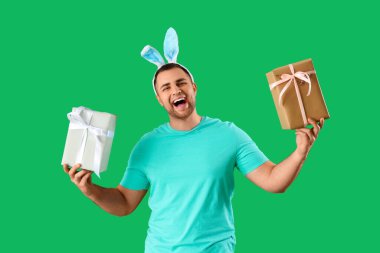 Yeşil arka planda hediye kutuları olan tavşan kulaklı mutlu genç adam. Paskalya kutlaması