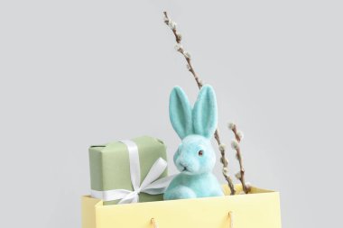 Shopping bag with toy Easter bunny, gift box and pussy willow branches on white background