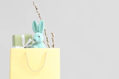 Shopping bag with toy Easter bunny, gift box and pussy willow branches on white background
