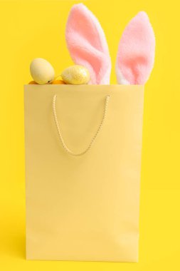 Sarı arka planda tüylü tavşan kulaklı ve Paskalya yumurtalı alışveriş torbası.