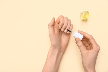 Bej arka planda fırçayla tırnak eti yağı süren kadın eller