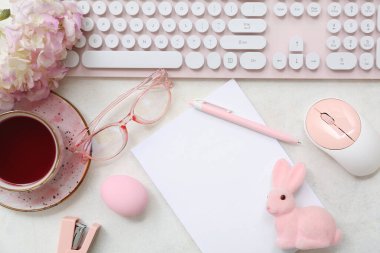 Boş kağıt çarşaf, cihazlar, bir fincan çay ve arka planda Paskalya dekoru olan kompozisyon