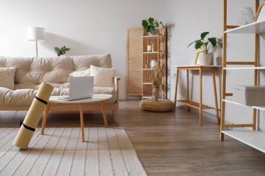 Oturma odasının içinde kanepe, yoga minderi ve dizüstü bilgisayar var.