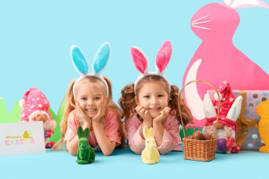 Paskalya tavşanları, yumurtalar ve mavi arka planda kağıt dekoru olan tavşan kulaklı şirin kızlar.