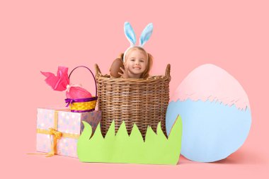Çikolatalı küçük kız sepette paskalya yumurtası ve pembe arka planda dekor.
