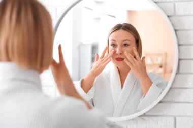 Kadın aynanın önünde yüz geliştirme egzersizi yapıyor.