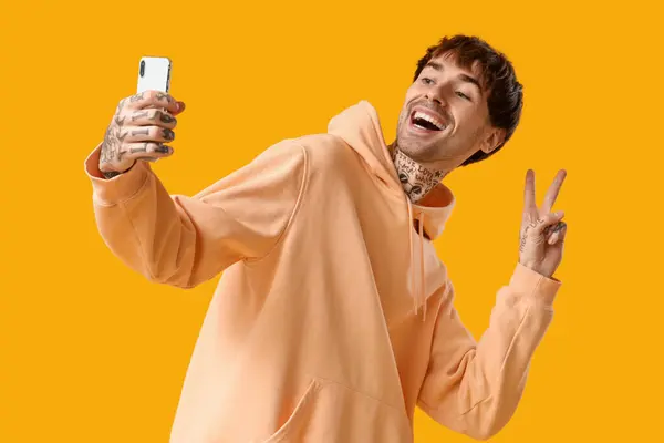 Młody Wytatuowany Mężczyzna Telefonem Robiący Selfie Żółtym Tle — Zdjęcie stockowe