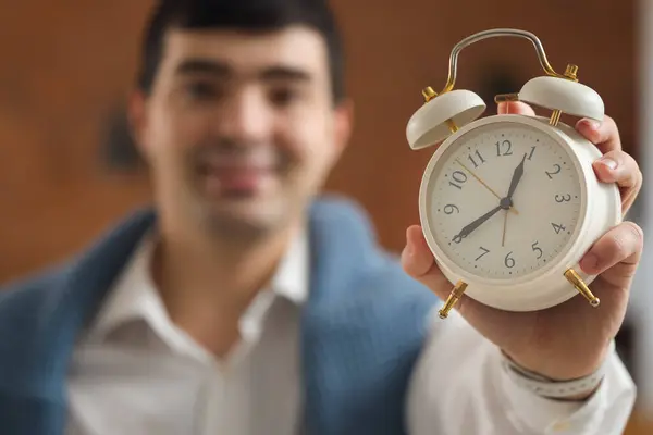 Young businessman with alarm clock in office, closeup