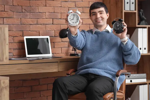 Young businessman with alarm clocks in office
