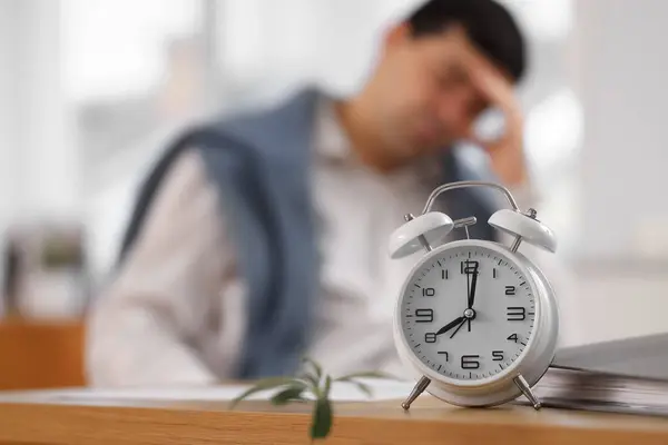 Alarm clock on table of stressed businessman in office, closeup