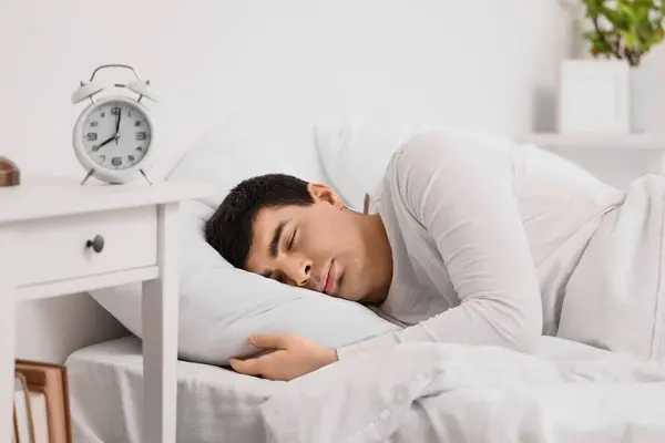 Young man with alarm clock sleeping in bedroom, closeup