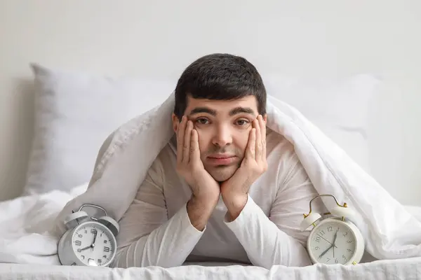 Young man with alarm clocks lying in bedroom, closeup