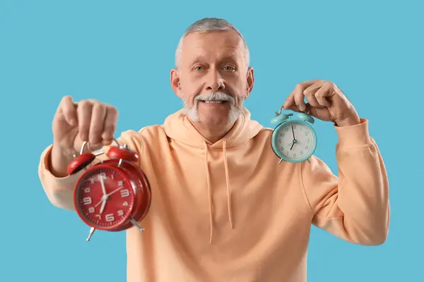 Mature man with alarm clocks on blue background