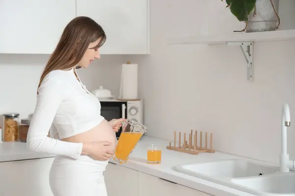Young pregnant woman pouring juice in kitchen