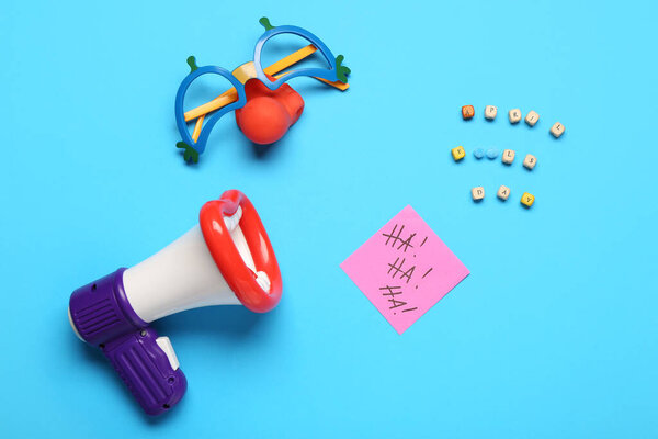 Text APRIL FOOLS DAY with megaphone, funny glasses and sticky note on blue background
