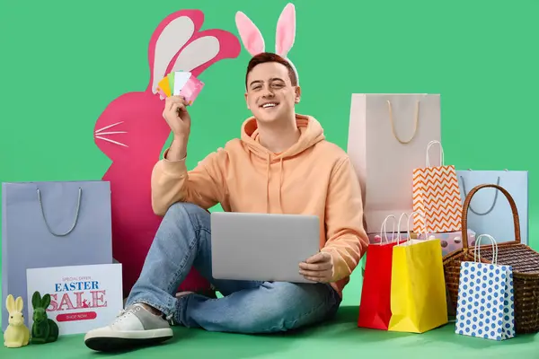 Junger Mann Hasenohren Mit Laptop Kreditkarten Und Einkaufstaschen Auf Grünem — Stockfoto