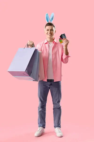 Junger Mann Hasenohren Mit Einkaufstaschen Und Kreditkarten Auf Rosa Hintergrund — Stockfoto