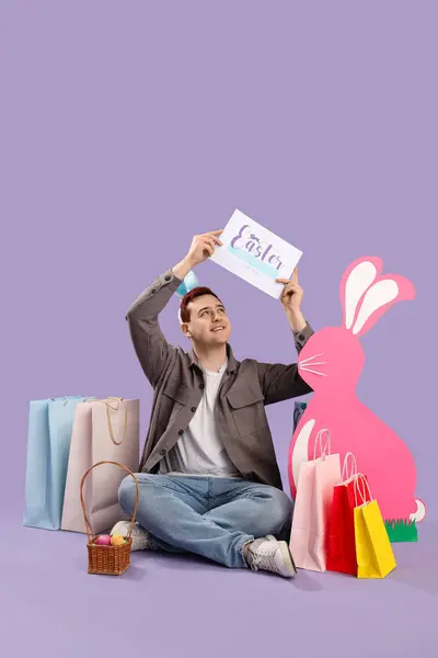 Junger Mann Hasenohren Mit Einkaufstaschen Und Dekor Auf Fliederfarbenem Hintergrund — Stockfoto