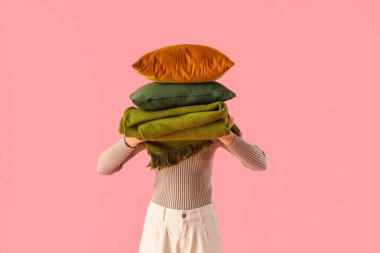 Yastık yığını ve pembe arka planda katlanmış sıcak ekoseli bir kadın.